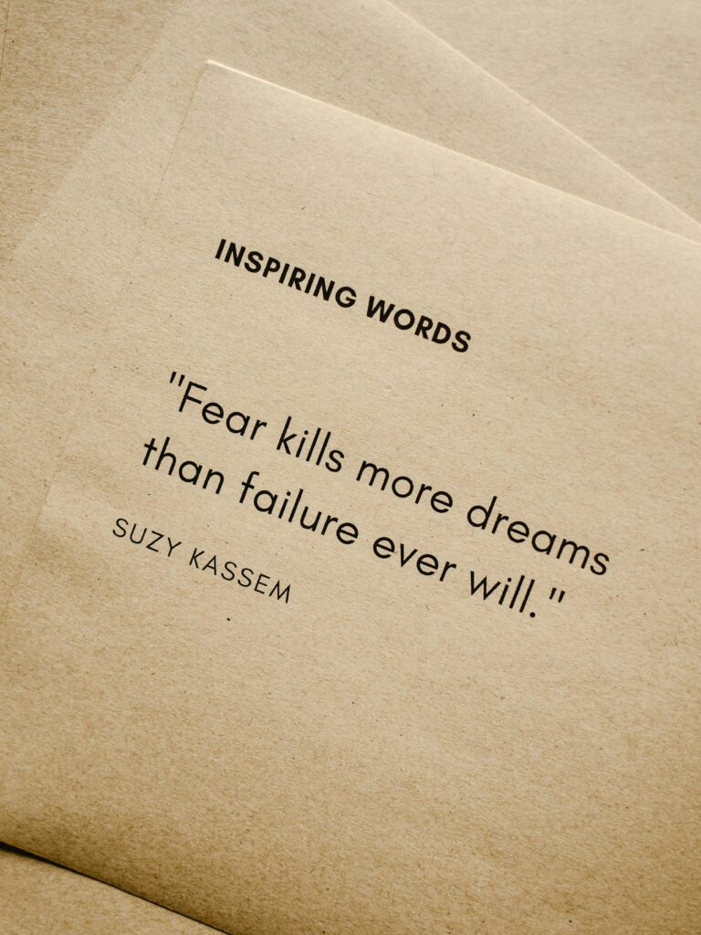 Motivational quote 'Fear kills more dreams than failure ever will.' by Suzy Kassem on paper texture.
