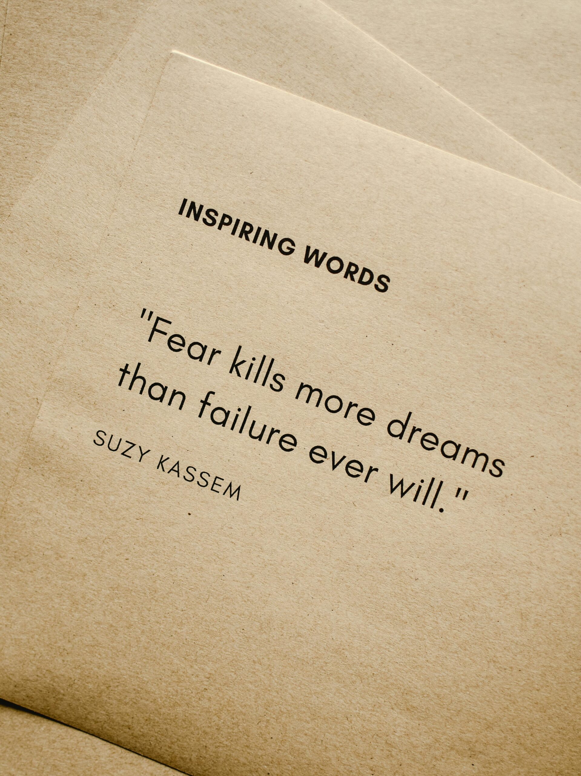 Motivational quote 'Fear kills more dreams than failure ever will.' by Suzy Kassem on paper texture.