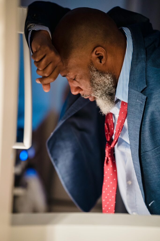 A tired businessman in a suit leans on a desk, depicting stress and exhaustion.