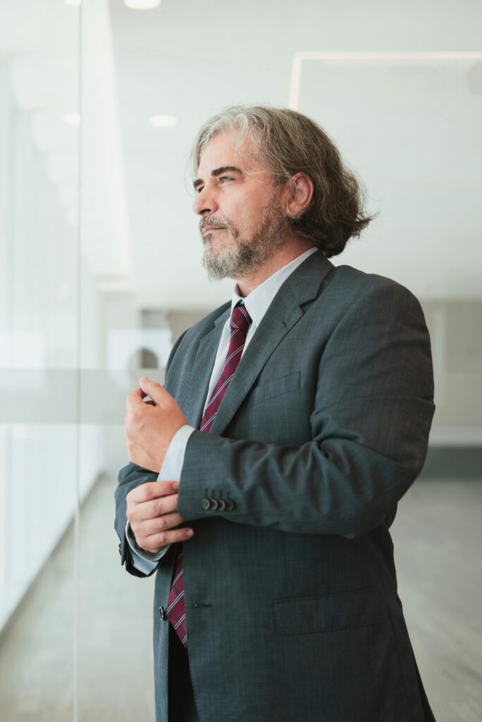 Businessman in a suit adjusting his cufflinks in a modern office space, exuding confidence.