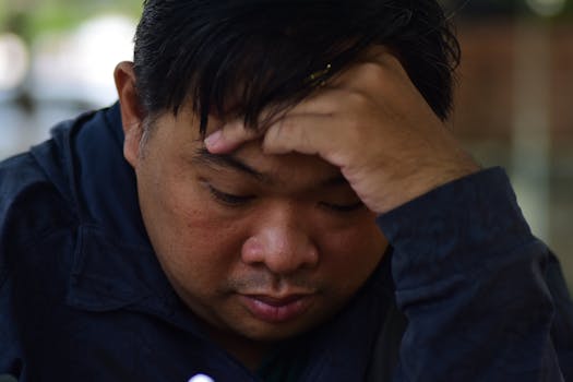 A man in deep thought with head resting on hand, captured in an indoor setting.